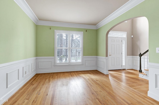 foyer featuring arched walkways, a wainscoted wall, crown molding, stairway, and light wood-type flooring