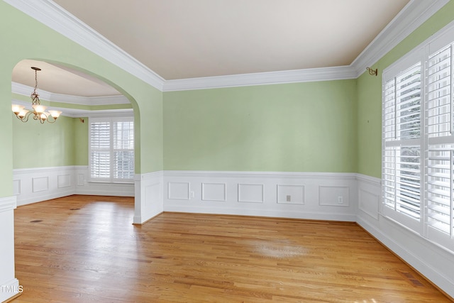 spare room featuring arched walkways, a chandelier, visible vents, light wood-style floors, and crown molding