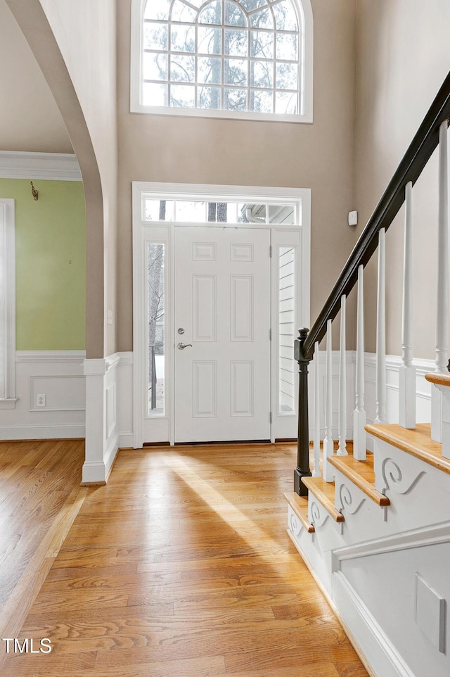 entrance foyer with light wood-style floors, arched walkways, a wainscoted wall, and plenty of natural light