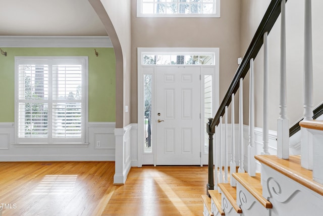 entrance foyer with arched walkways, ornamental molding, wainscoting, and light wood-style flooring