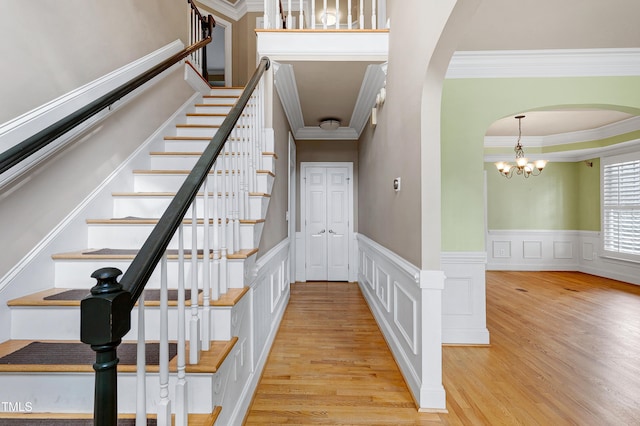 staircase with ornamental molding, arched walkways, an inviting chandelier, and wood finished floors