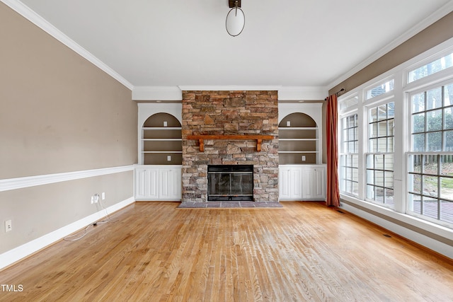 unfurnished living room with built in features, ornamental molding, a stone fireplace, wood finished floors, and baseboards