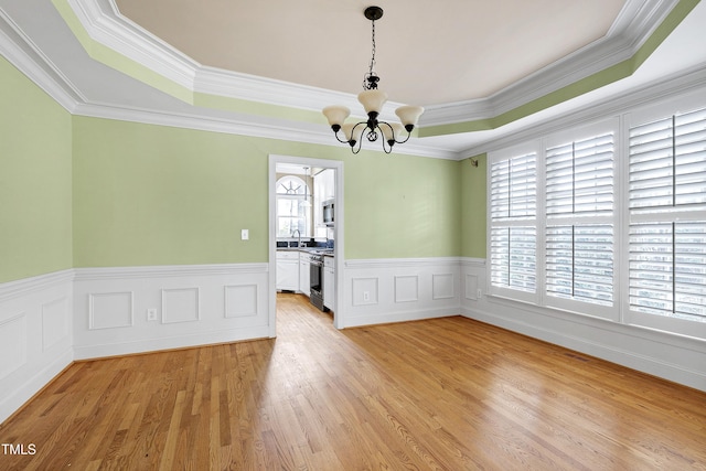 unfurnished dining area with wainscoting, a raised ceiling, light wood-style flooring, and an inviting chandelier