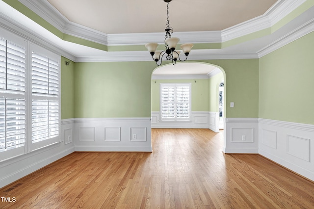 unfurnished dining area featuring arched walkways, crown molding, a notable chandelier, light wood finished floors, and a raised ceiling