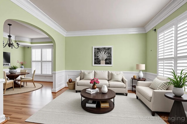 living room featuring an inviting chandelier, ornamental molding, wainscoting, and wood finished floors