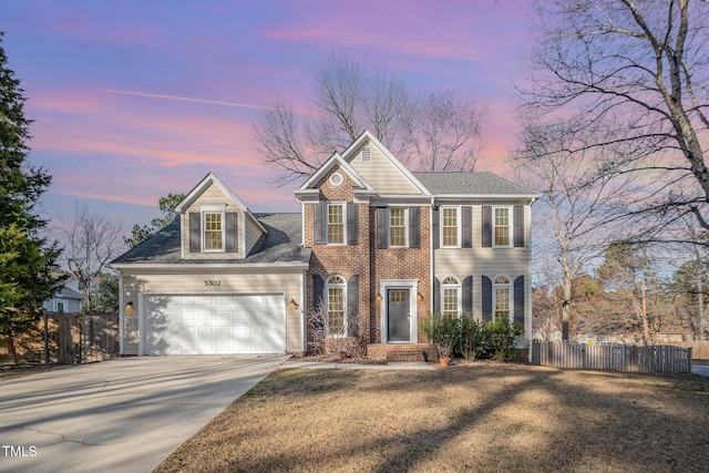 colonial inspired home featuring brick siding, concrete driveway, a yard, an attached garage, and fence