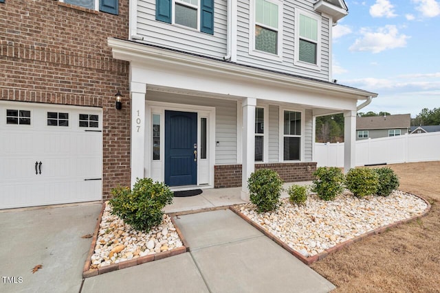 doorway to property featuring a garage, brick siding, covered porch, and fence