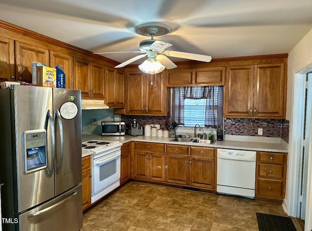 kitchen with brown cabinets, a sink, under cabinet range hood, stainless steel appliances, and decorative backsplash