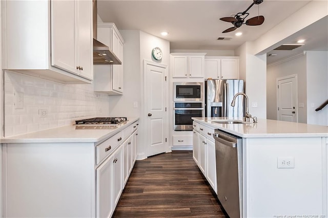 kitchen with a center island with sink, sink, white cabinetry, stainless steel appliances, and wall chimney exhaust hood