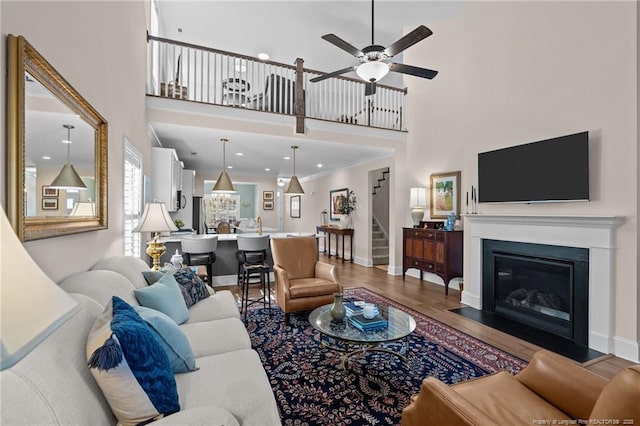 living room featuring a high ceiling, hardwood / wood-style flooring, crown molding, and ceiling fan