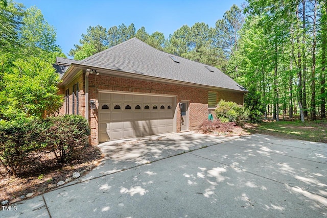 view of side of home with concrete driveway, brick siding, an attached garage, and roof with shingles