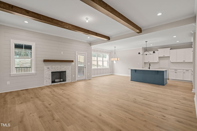 unfurnished living room with light wood-style flooring, a fireplace, baseboards, beam ceiling, and crown molding