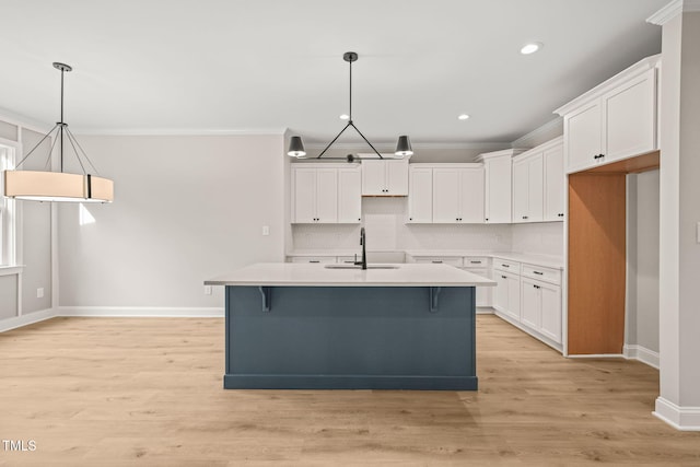 kitchen with light wood-style flooring, a kitchen island with sink, a sink, ornamental molding, and tasteful backsplash