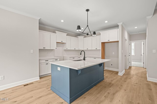 kitchen with white cabinets, a sink, light wood finished floors, and a center island with sink
