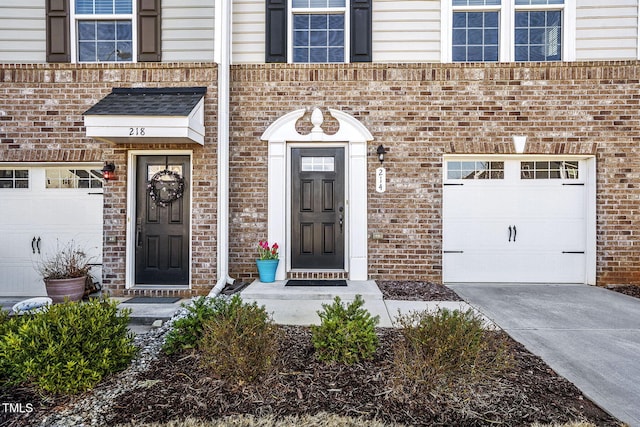 entrance to property featuring a garage, concrete driveway, and brick siding