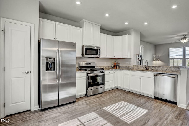 kitchen featuring light wood-style flooring, appliances with stainless steel finishes, light stone counters, white cabinetry, and a sink