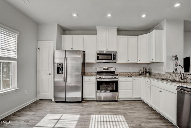 kitchen with light stone counters, appliances with stainless steel finishes, a sink, and white cabinetry