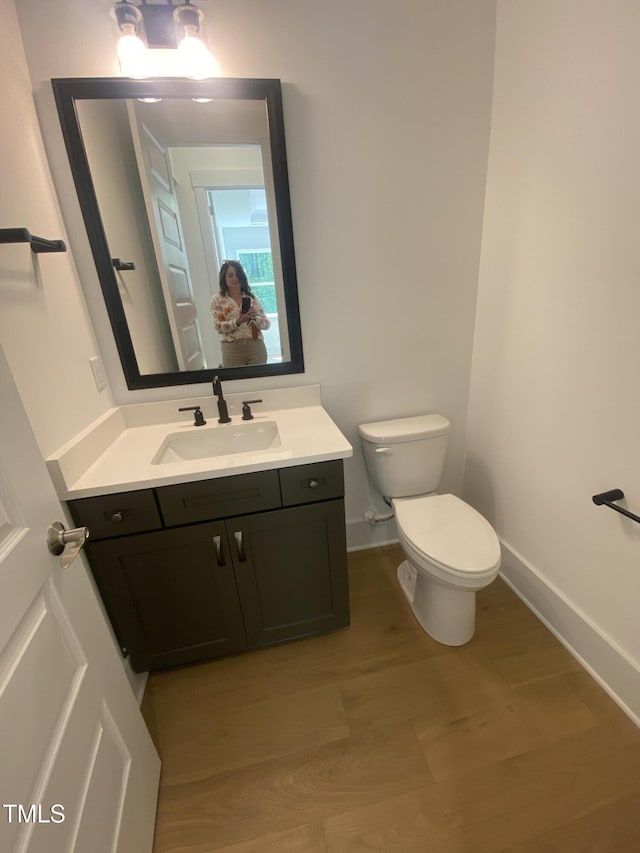 half bathroom featuring toilet, baseboards, wood finished floors, and vanity