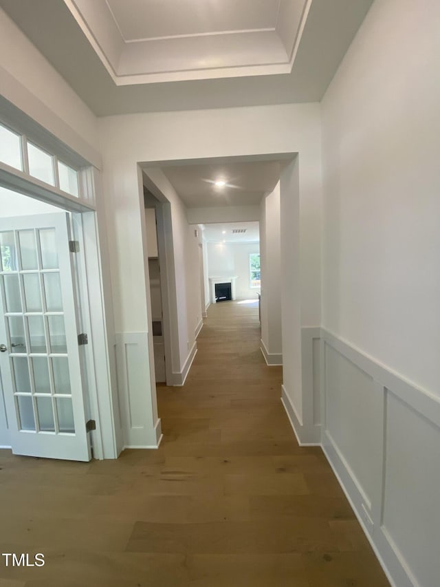 hall featuring a raised ceiling, a decorative wall, wood finished floors, and a wainscoted wall