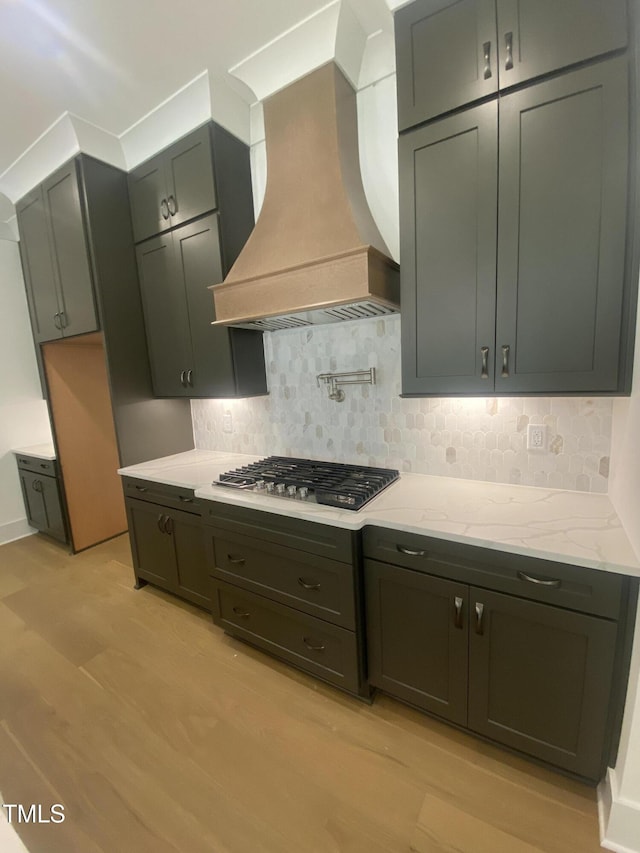 kitchen featuring premium range hood, stainless steel gas cooktop, backsplash, and light stone counters