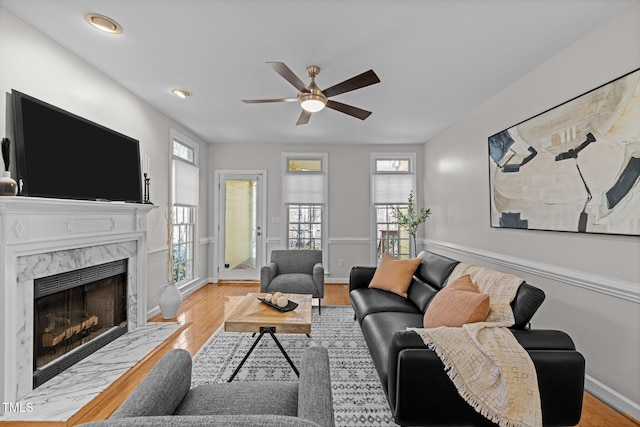 living room featuring baseboards, a high end fireplace, light wood-style flooring, and a healthy amount of sunlight