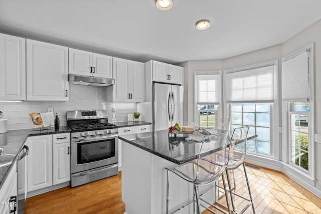 kitchen with appliances with stainless steel finishes, white cabinetry, a kitchen island, dark stone countertops, and under cabinet range hood