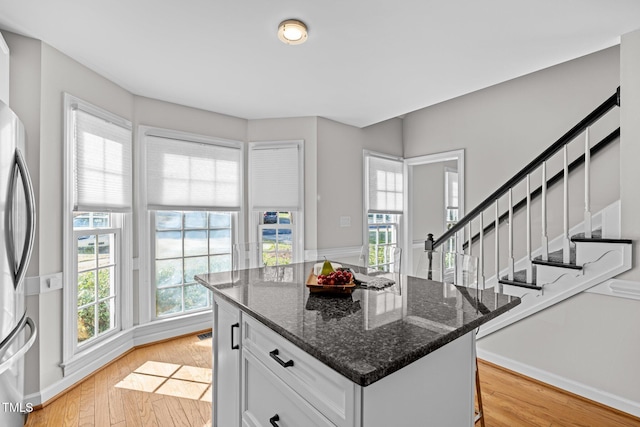 kitchen with light wood-style flooring, a kitchen island, white cabinetry, freestanding refrigerator, and dark stone countertops