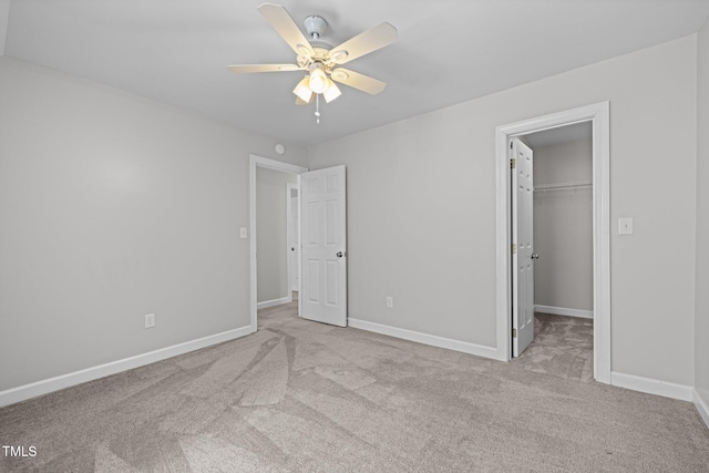 unfurnished bedroom featuring a closet, light carpet, a spacious closet, and baseboards