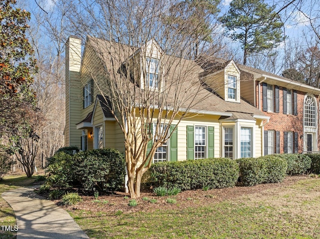 view of front of home featuring roof with shingles, a front lawn, and a chimney