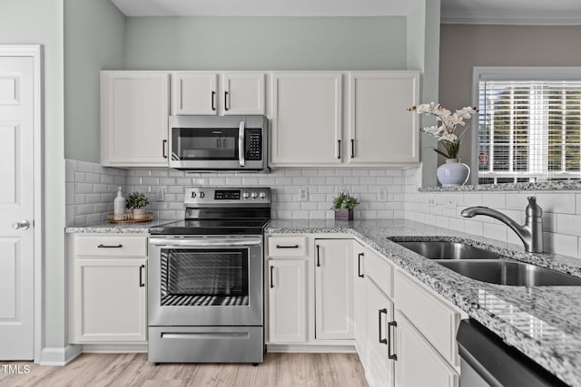 kitchen with light stone countertops, white cabinetry, stainless steel appliances, and a sink