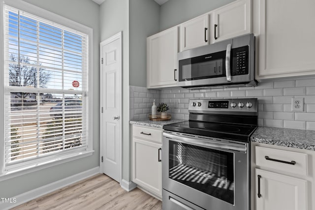 kitchen featuring a wealth of natural light, appliances with stainless steel finishes, white cabinets, and light stone counters