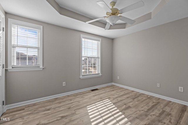 spare room with a tray ceiling, visible vents, light wood-style floors, ceiling fan, and baseboards