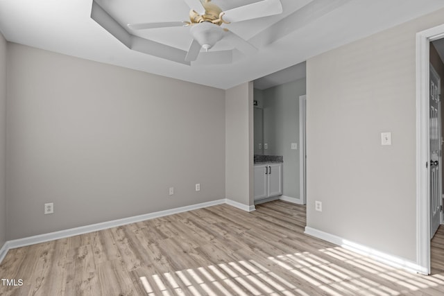 unfurnished bedroom featuring light wood-style floors, ceiling fan, baseboards, and a raised ceiling