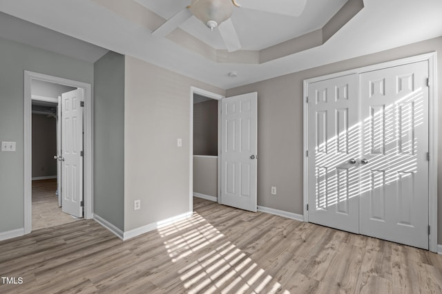 unfurnished bedroom featuring a ceiling fan, baseboards, a closet, light wood finished floors, and a raised ceiling