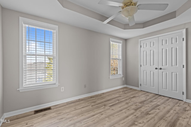 unfurnished bedroom with light wood-type flooring, a tray ceiling, visible vents, and baseboards