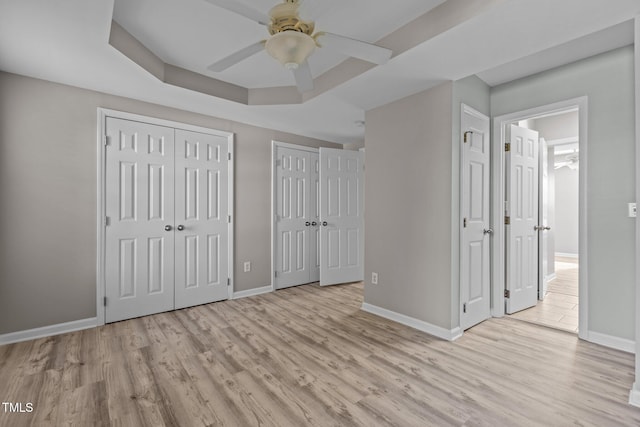 unfurnished bedroom with light wood finished floors, a raised ceiling, two closets, and baseboards