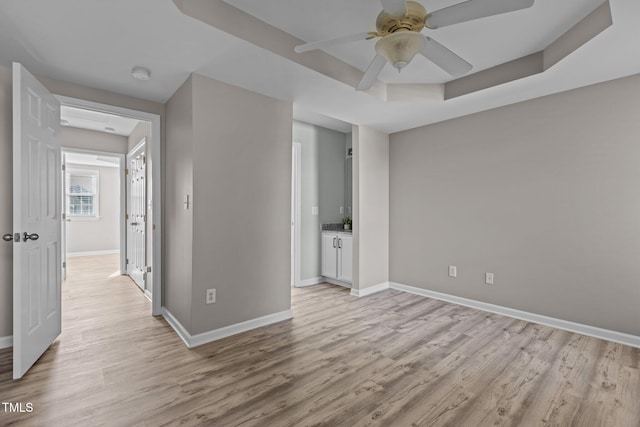 empty room with light wood finished floors, a raised ceiling, a ceiling fan, and baseboards