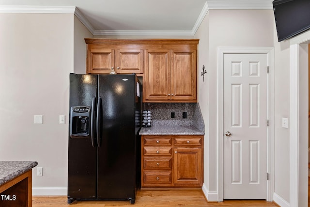 kitchen featuring light wood-type flooring, tasteful backsplash, light stone counters, crown molding, and black fridge