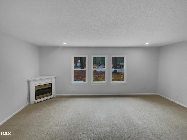 unfurnished living room featuring baseboards, light colored carpet, a glass covered fireplace, a textured ceiling, and recessed lighting