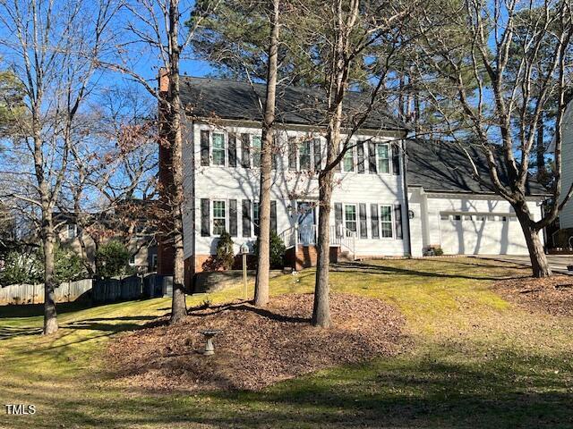 colonial home with a garage, a front lawn, a chimney, and fence