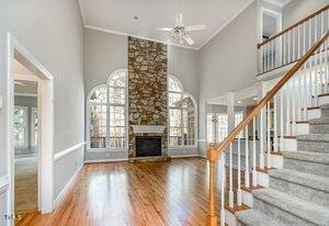 unfurnished living room with a fireplace, stairway, ceiling fan, wood finished floors, and high vaulted ceiling