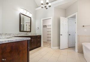 bathroom featuring lofted ceiling, tile patterned flooring, vanity, a freestanding tub, and a chandelier