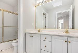 bathroom with bath / shower combo with glass door, double vanity, toilet, a sink, and tile patterned flooring