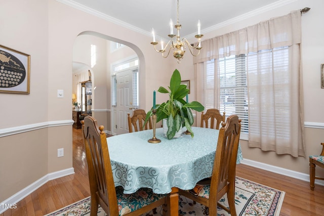 dining area featuring baseboards, arched walkways, crown molding, and wood finished floors