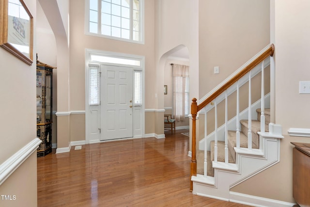 foyer with a towering ceiling, plenty of natural light, arched walkways, and wood finished floors