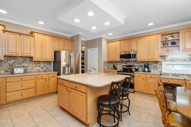 kitchen featuring a kitchen breakfast bar, light countertops, appliances with stainless steel finishes, light brown cabinetry, and an island with sink