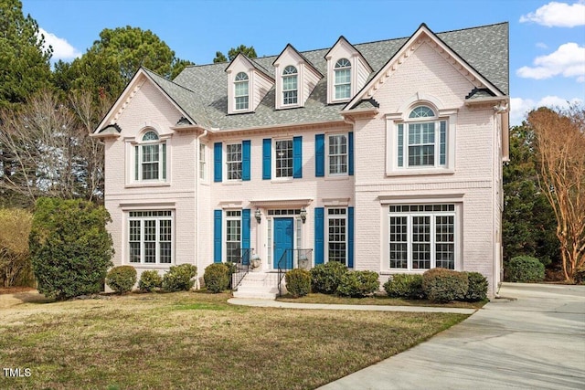 view of front facade with a shingled roof, a front yard, and brick siding