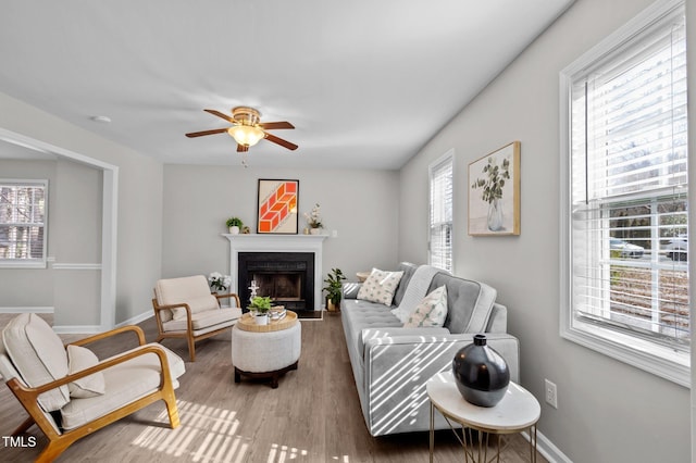 living area featuring a ceiling fan, a fireplace, baseboards, and wood finished floors