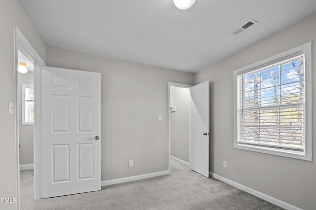 unfurnished bedroom with visible vents, light carpet, baseboards, and multiple windows