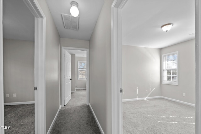 hall with baseboards, visible vents, dark colored carpet, and a wealth of natural light